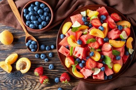 delicious colorful fresh fruit salad with watermelon, blueberries, peach slices, strawberry and lime on a clay plate on an old rustic table with ingredients, horizontal view from above, flatlay